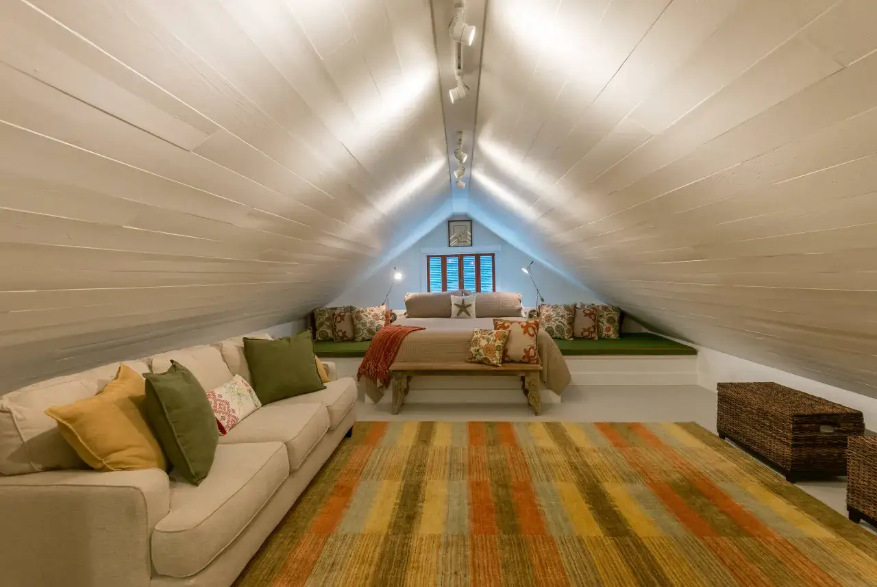 Przytulna sypialnia na poddaszu z kanapą, ł&oacute;żkiem i kolorowym dywanem. Led&oacute;w na skosach dodają ciepłego blasku.