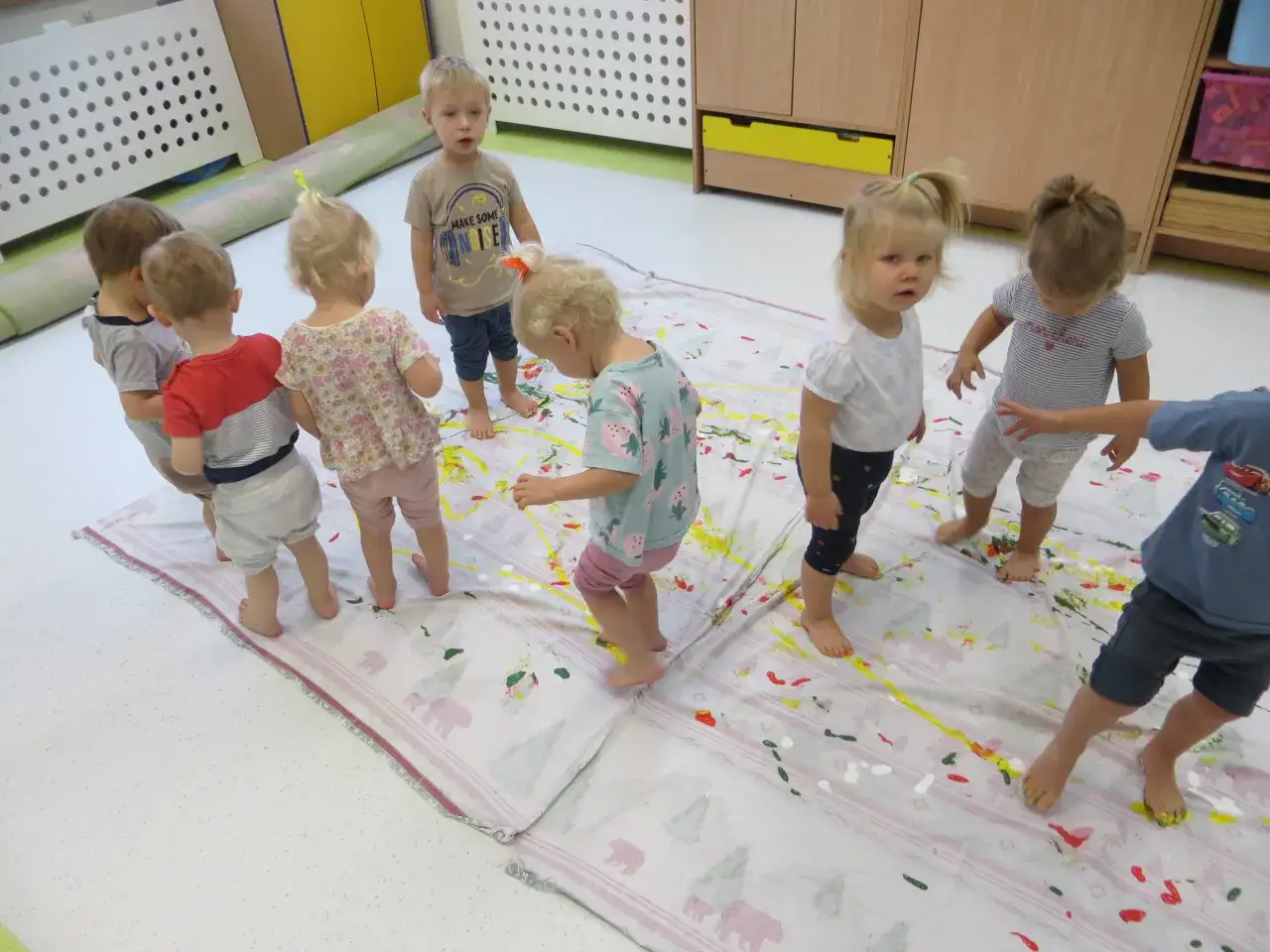 Dzieci malują stopami na wielkim płótnie, tworząc kolorowy bałagan. Tak wygląda radosny żłobek.