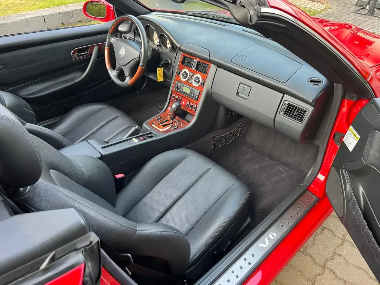 Wnętrze czerwonego Mercedesa Benz SLK z czarną skórzaną tapicerką i drewnianymi wstawkami. Widoczna kierownica, deska rozdzielcza i fotele.