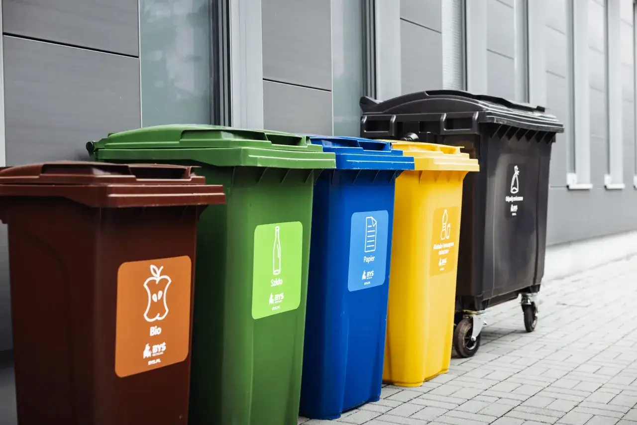 Kolorowe pojemniki na śmieci, wykonane z tworzywa sztucznego, stoją obok siebie. Brązowy na bio, zielony na szkło, niebieski na papier, ż&oacute;łty na metale i tworzywa sztuczne, czarny na odpady zmieszane.