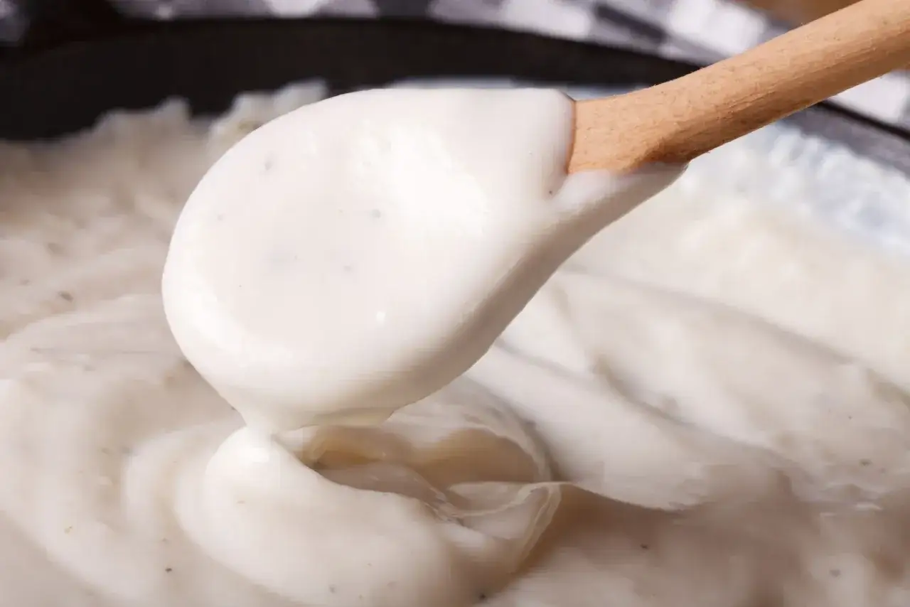 Gładki, kremowy sos beszamelowy na drewnianej łyżce, gotowy do polania lasagne.