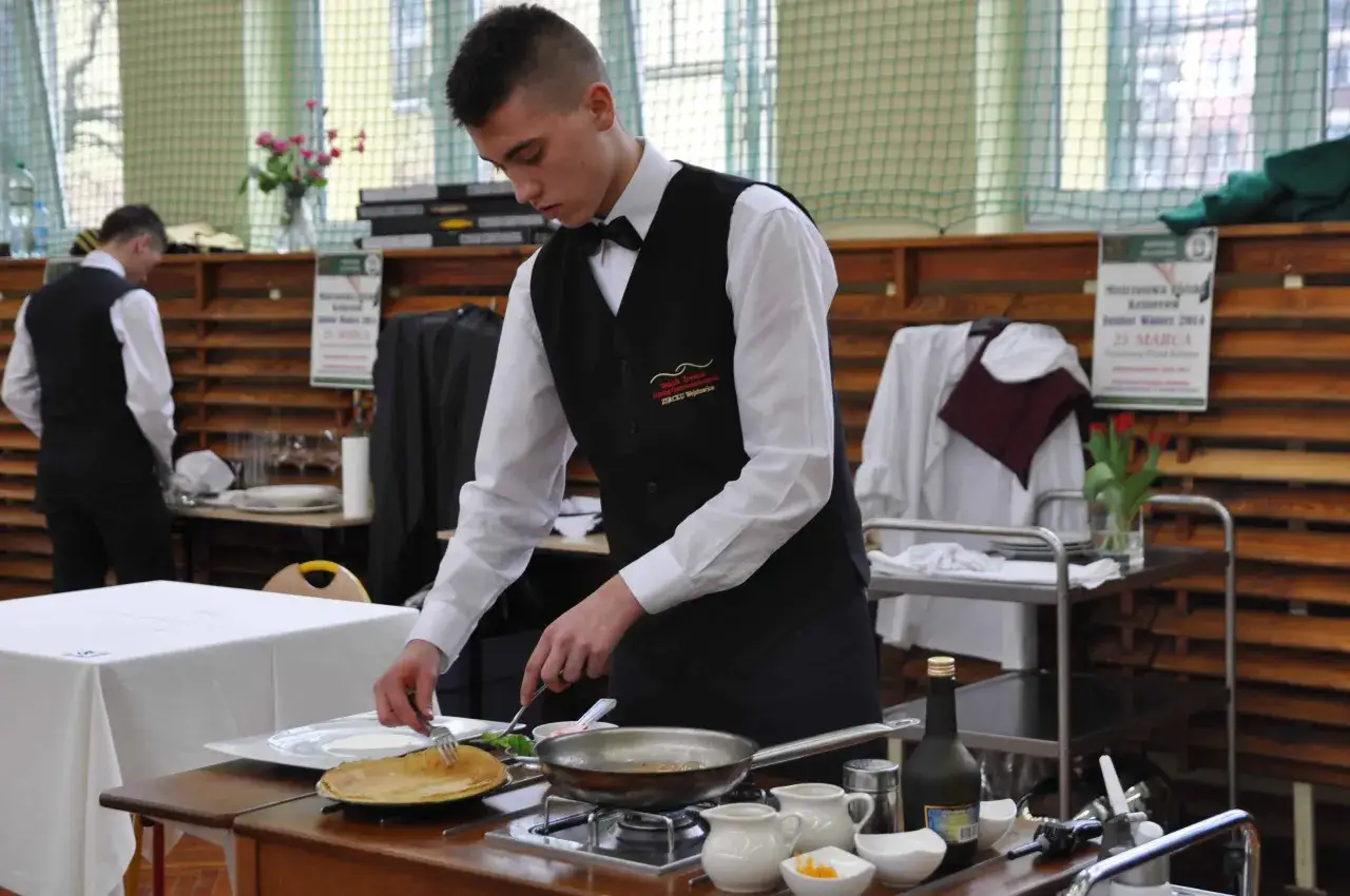 Młody kucharz przygotowuje naleśniki. Zastanawiasz się, ile kosztuje kurs kelnerski?