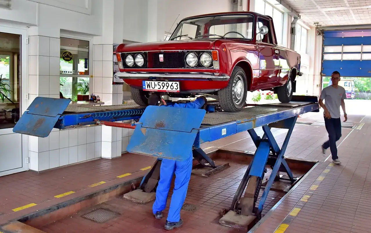 Mechanik pracuje pod czerwonym Fiatem 125p na podnośniku. Czy rejestracja na zabytek plusy i minusy są warte zachodu?