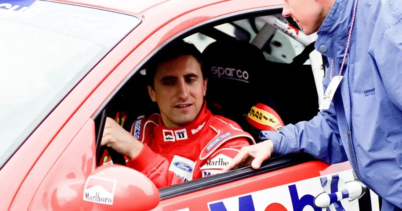 Janusz Kulig w czerwonym kombinezonie rajdowym, w aucie Ford Focus. Rozmowa z mechanikiem, może to początek romansu z rajdami?