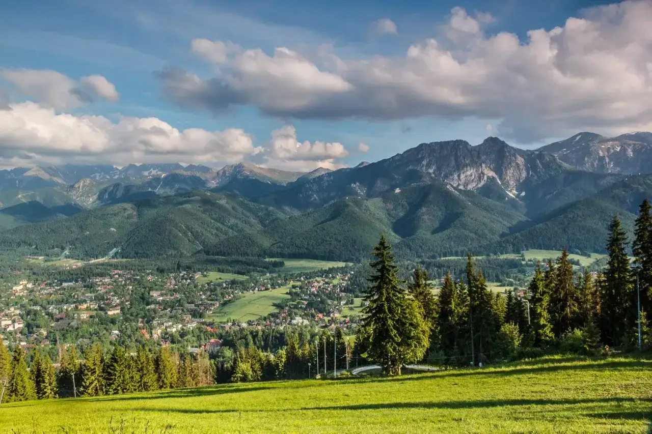 Zielona dolina z miasteczkiem i lasami, na horyzoncie majestatyczne, skaliste g&oacute;ry. Tak wyglądają g&oacute;ry w pełnej krasie.