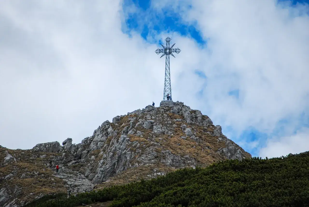 Szczyt Giewontu z krzyżem, na który wspina się kilku turystów. Wysokość Giewontu to 1894 m n.p.m.