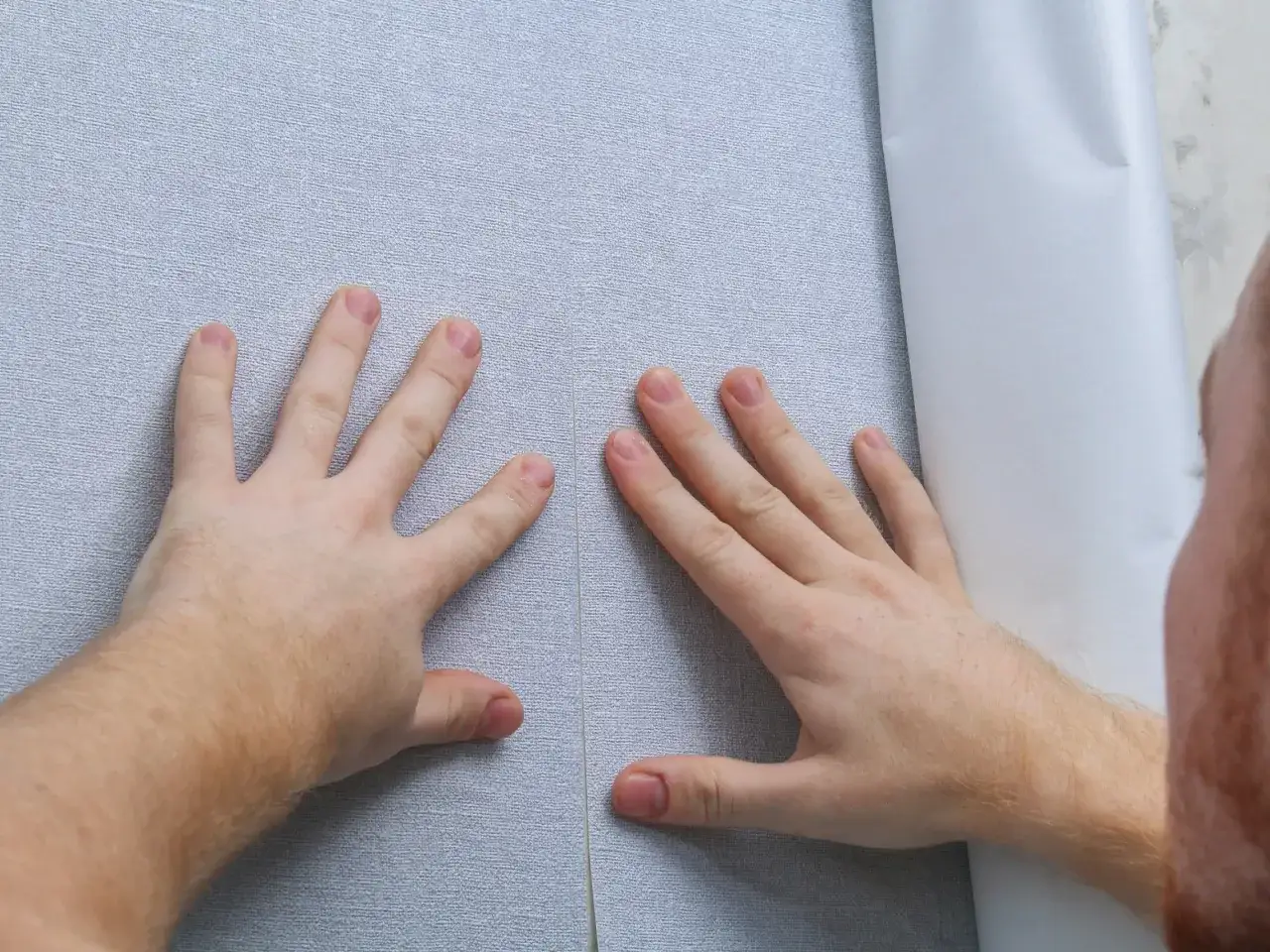 Dłonie próbują wyrównać tapetę, ale widać wyraźne błędy przy tapetowaniu – nierówne połączenie pasów.