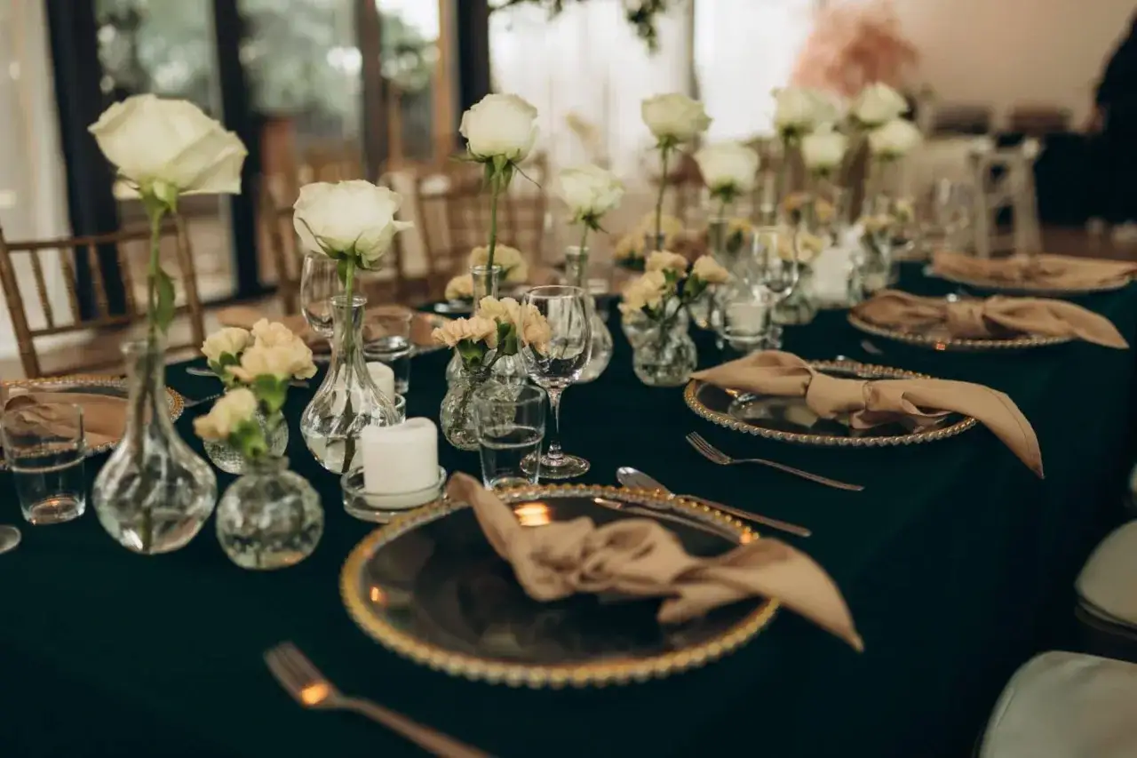 Eleganckie wesele w stylu glamour: złote talerze, białe róże i beżowe serwetki. Kontrastuje z nowoczesnym minimalizmem.