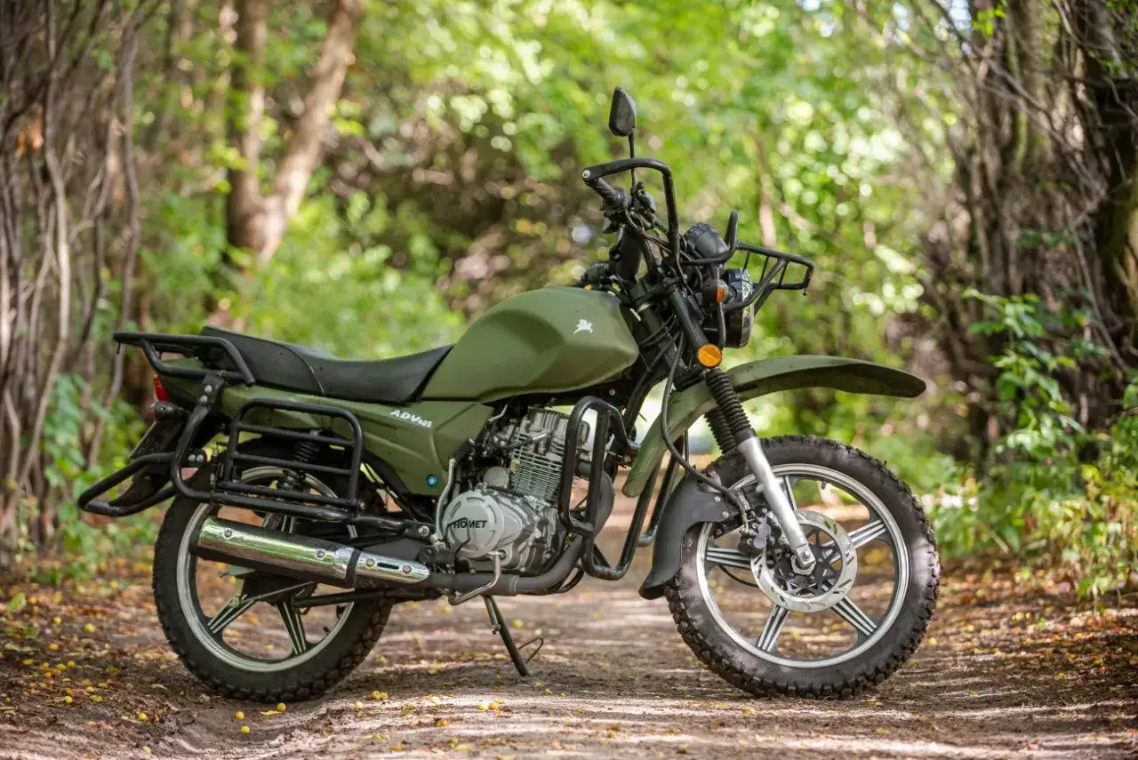 Zielony Romet Scrambler 125 ADV stoi na leśnej ścieżce, gotowy na przygodę.