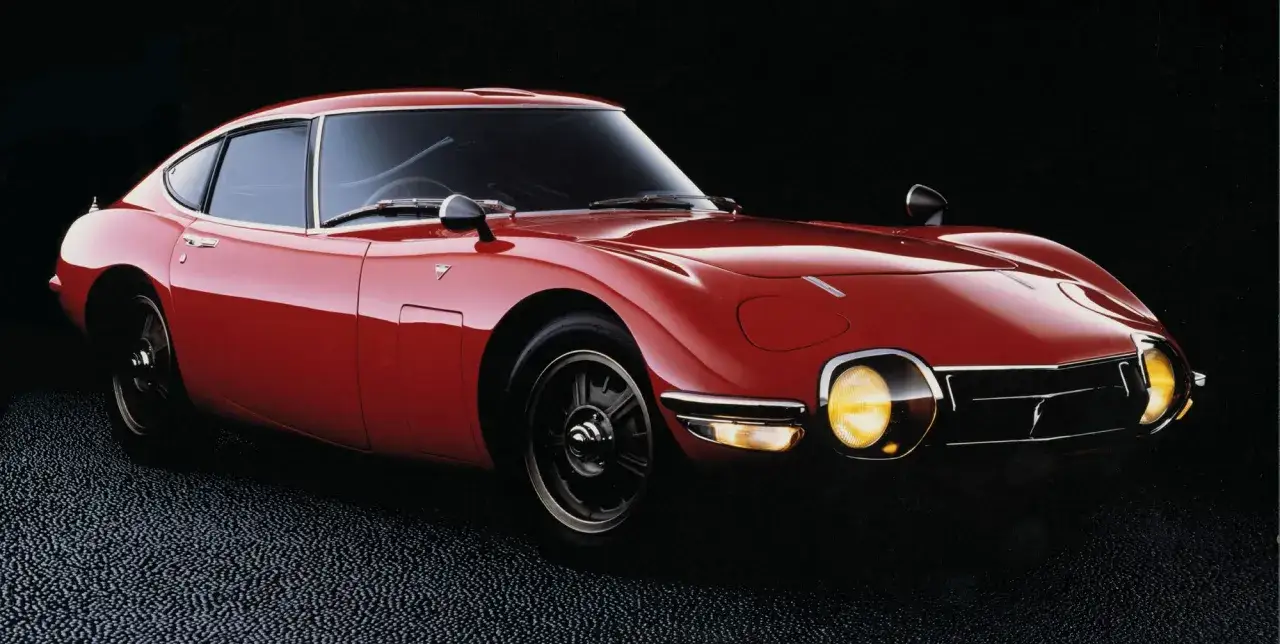 Klasyczny, czerwony Toyota 2000GT, jeden z najbardziej ikonicznych japońskich samochodów sportowych, błyszczy na czarnym tle.