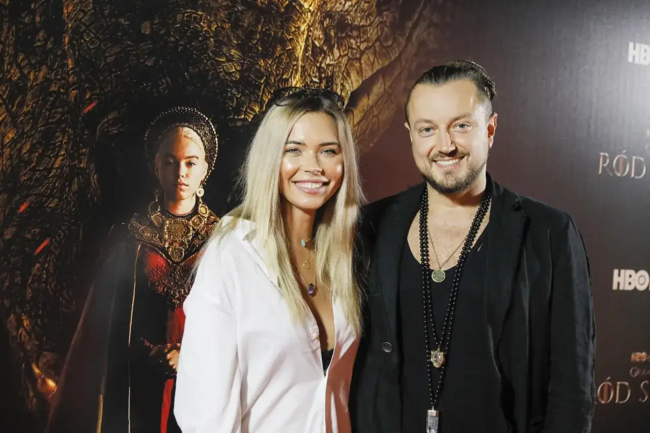 Uśmiechnięty baron z żoną pozują na tle smoka i postaci z serialu.