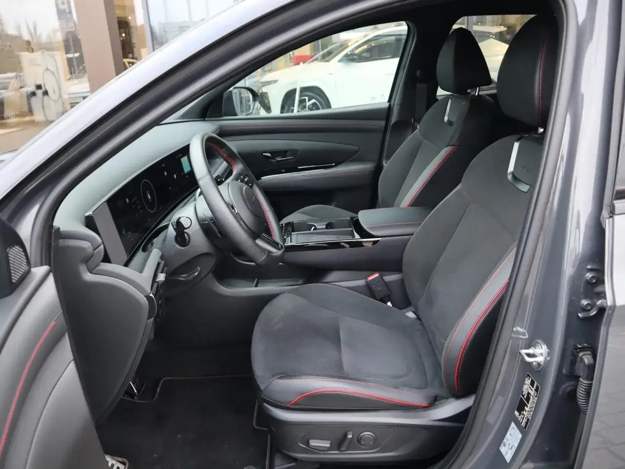 Wnętrze nowoczesnego auta z czarnymi fotelami i czerwonymi przeszyciami. Kierownica i deska rozdzielcza z ekranem. Zastanawiasz się, o co pytać przy zakupie auta?