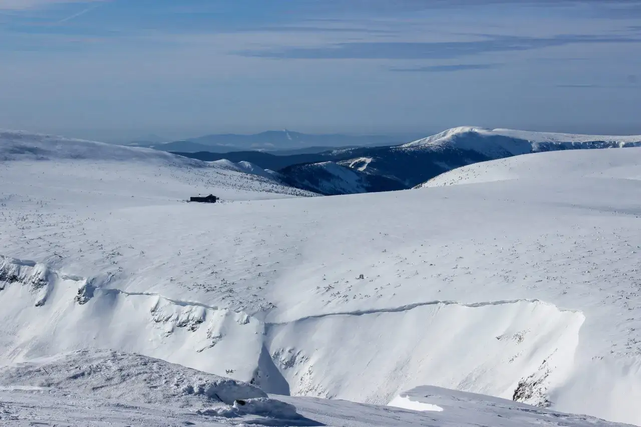 Zimowy krajobraz g&oacute;rski z chatką na przełęczy okraj. W oddali widać kolejne pasma g&oacute;rskie.