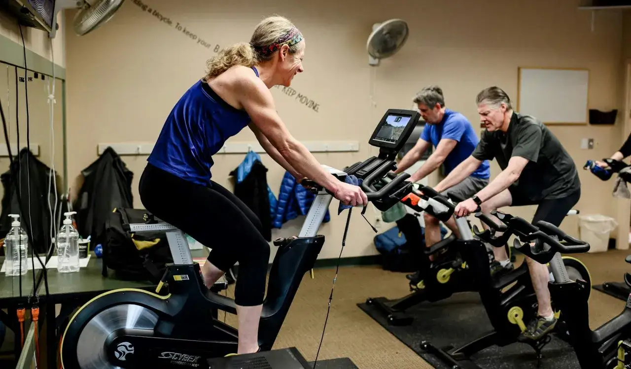 Intensywny trening spinningowy w sali fitness. Kobieta w niebieskiej koszulce i mężczyźni na rowerach stacjonarnych.