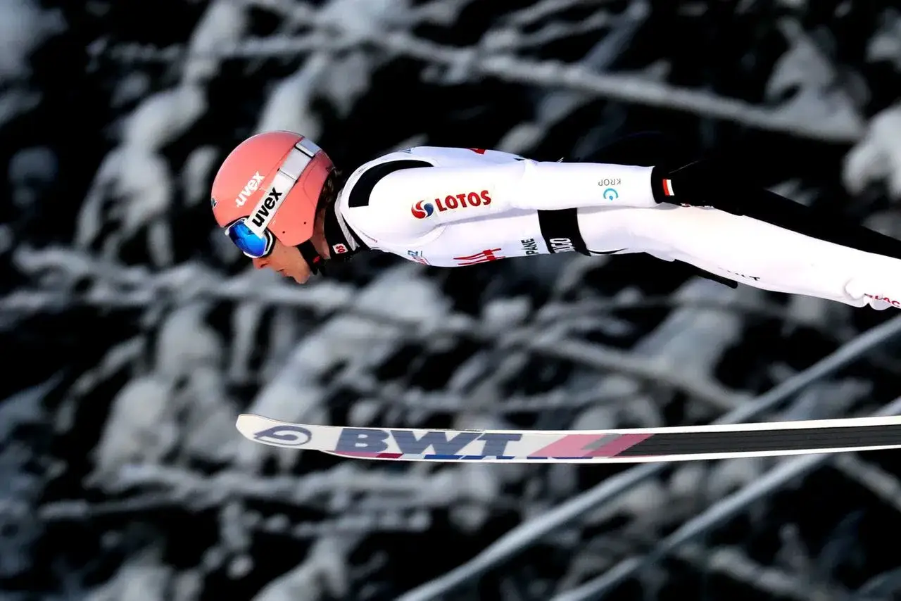 Skoczek narciarski w locie, w białym kombinezonie z logo LOTOS. Zastanawiasz się, ile musi ważyć skoczek narciarski, by osiągnąć taki dystans?