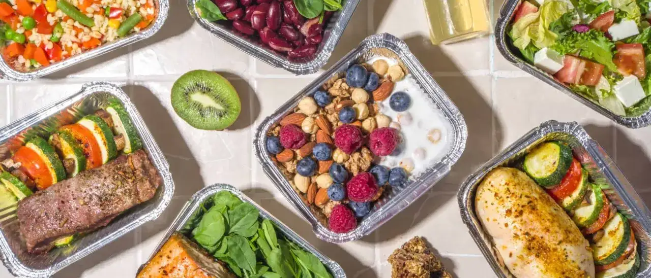 Różnorodne dania w pojemnikach: mięso, ryba, sałatka, owoce, orzechy. To przykład, co to catering dietetyczny – zdrowe posiłki na wynos.