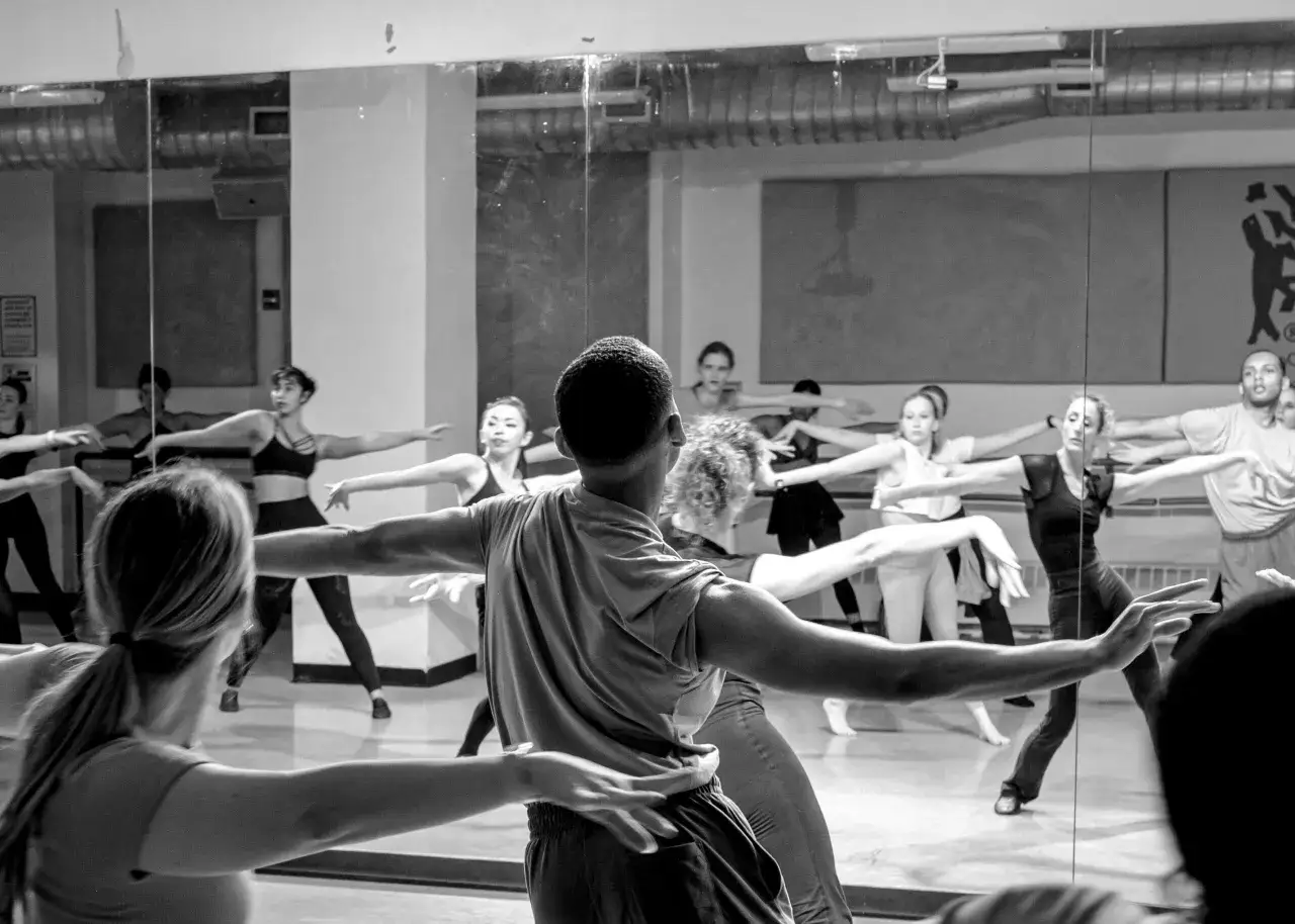 Grupa tancerzy ćwiczy nowoczesny taniec jazzowy w sali z lustrami.