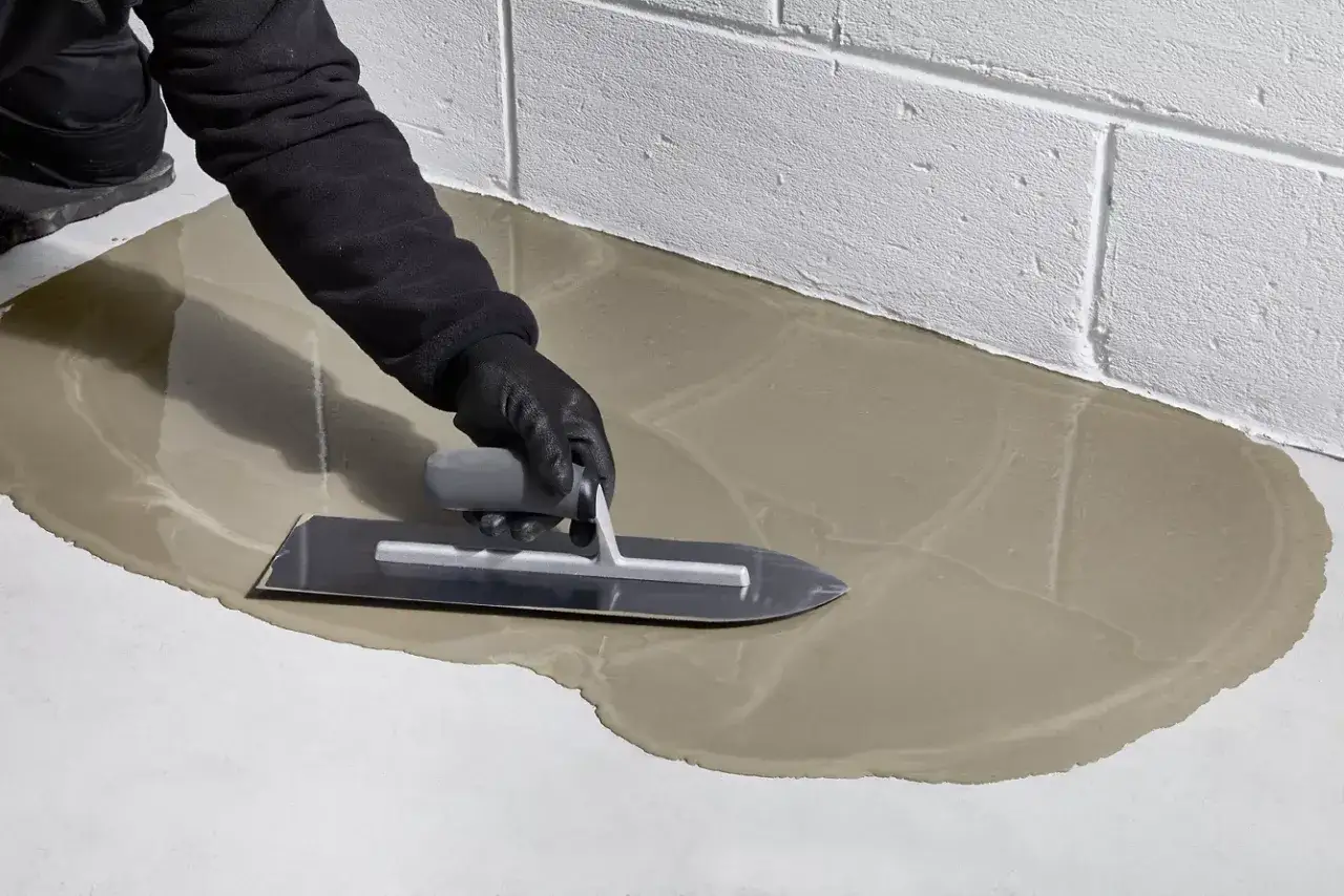 Ręka w rękawicy wygładza świeżą wylewkę betonową kielnią. Dowiedz się, jak zrobić wylewkę betonową krok po kroku.