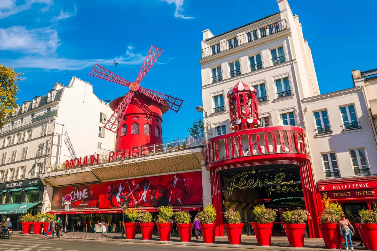 Moulin Rouge, ikona 18. dzielnicy Paryża, lśni w słońcu. Czerwony wiatrak i neonowy napis zapraszają na niezapomniane widowisko.