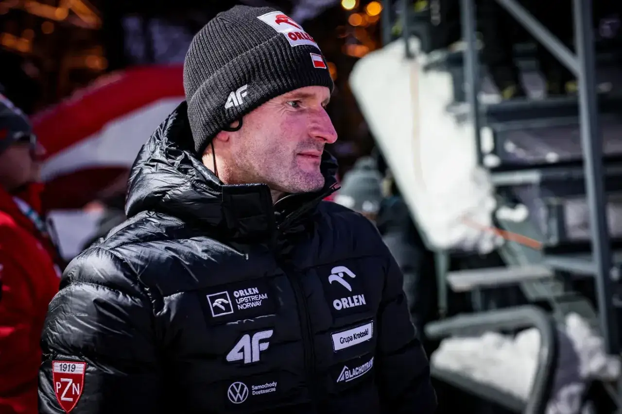 Trener polskich skoczków, w czapce z flagą Polski, w zimowej kurtce z logo ORLEN.