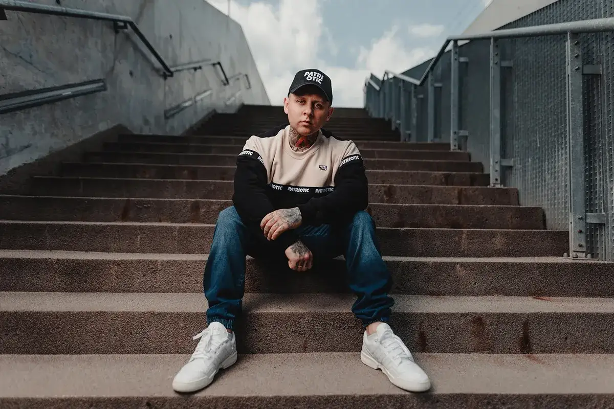 Chłopak w czapce z daszkiem i bluzie z kapturem, dżinsach i białych sneakersach. Idealny strój, jak się ubrać na koncert hip hopowy.