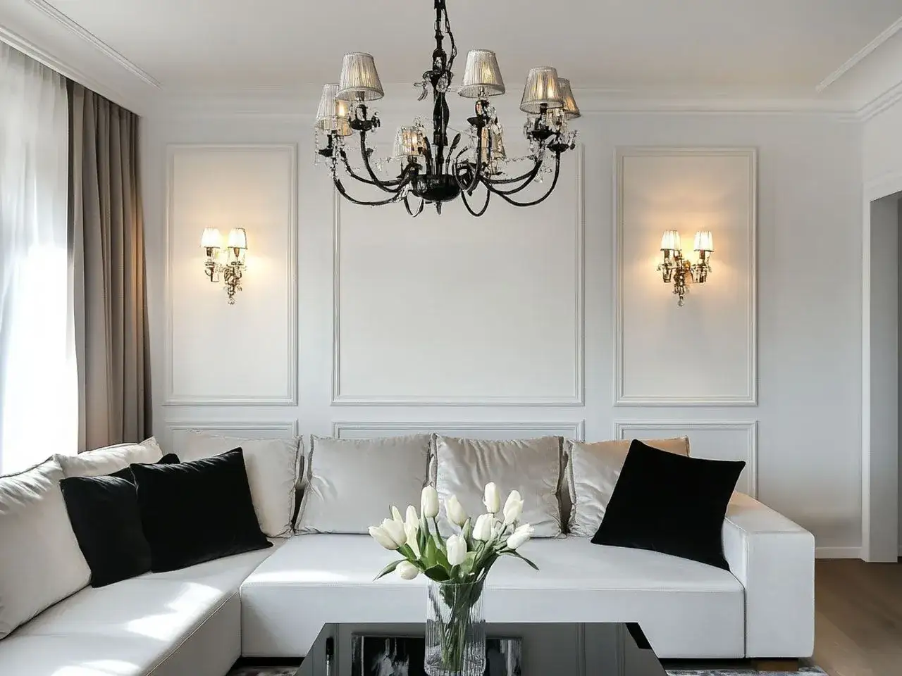 Elegancka ściana glamour w salonie z białym narożnikiem, czarnymi i beżowymi poduszkami, kryształowym żyrandolem i wazonem z tulipanami.