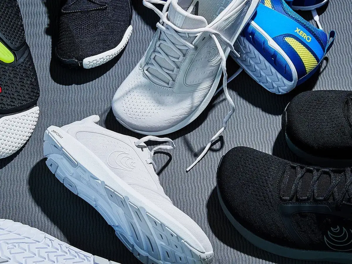 R&oacute;żne modele but&oacute;w sportowych, w tym białe i czarne, niekt&oacute;re z technologią 0 drop, leżą na szarej macie.