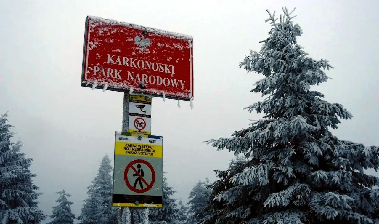 Znak Karkonoskiego Parku Narodowego w zimowej scenerii. Czy szlaki turystyczne są otwarte? Tablice informują o zakazie wstępu i lot&oacute;w dronem.