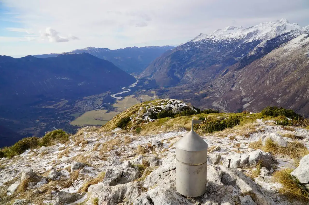 Majestatyczne g&oacute;ry w Bułgarii, dolina z rzeką i ośnieżone szczyty. Na pierwszym planie metalowy obiekt i kamienie.