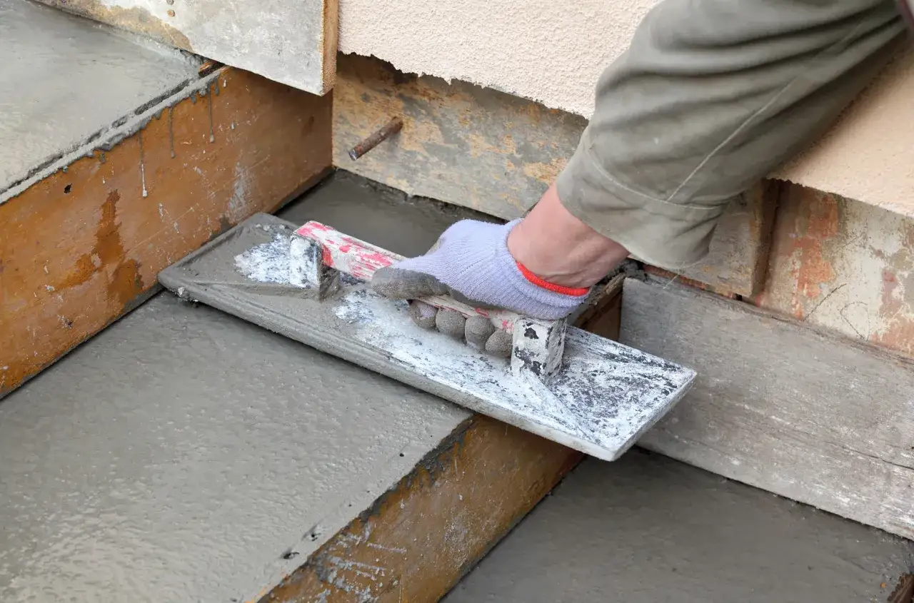Ręka w rękawicy wygładza świeży beton, pokazując, jak zrobić schody betonowe.
