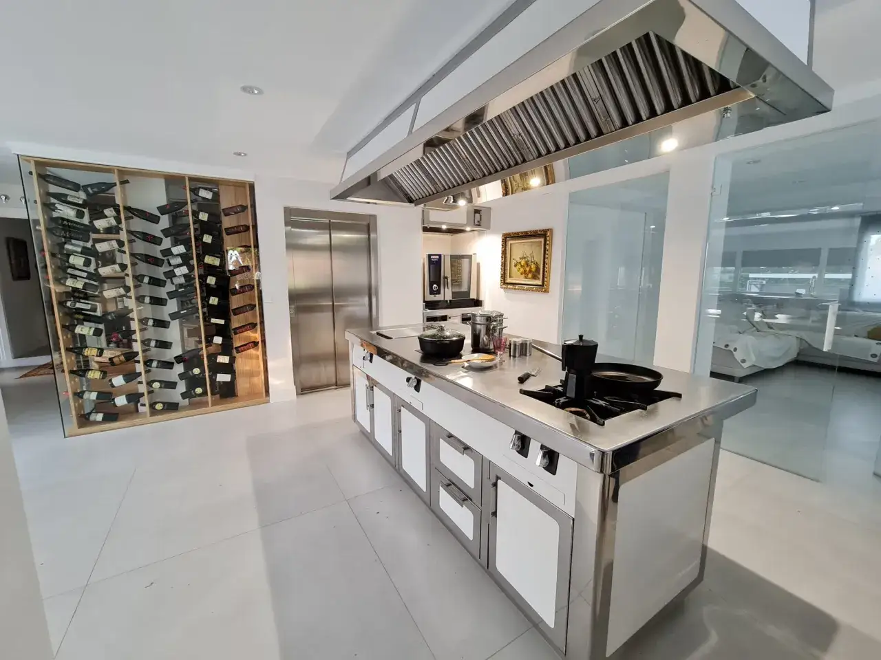 Cocina moderna con isla central de acero inoxidable, vinoteca y ascensor. Muebles de cocina fabricantes de alta gama.