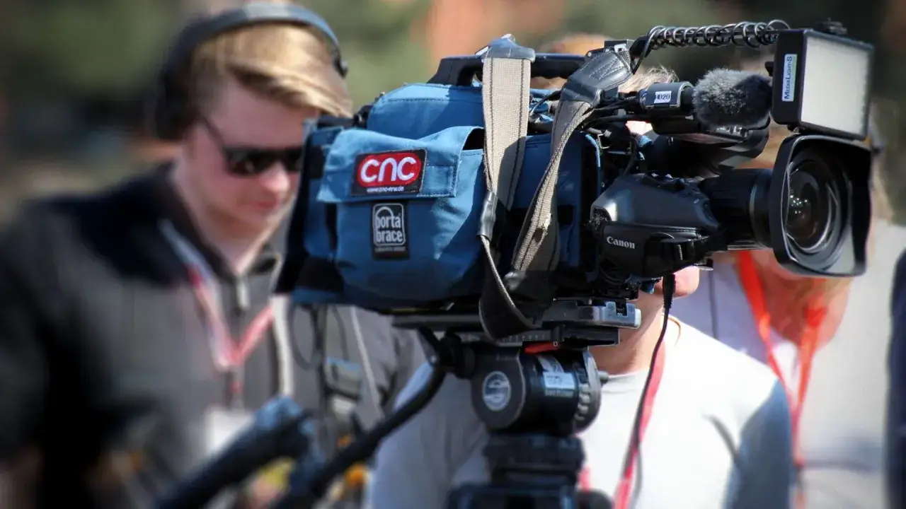 Producenci na planie filmowym pracują z profesjonalnym sprzętem. Widać kamerę Canon, mikrofon i lampę.