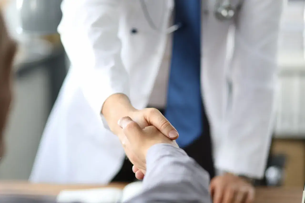 Lekarz w białym kitlu ściska dłoń pacjenta. Szukasz, gdzie najszybciej rehabilitacja NFZ CzęSTOCHOWA?