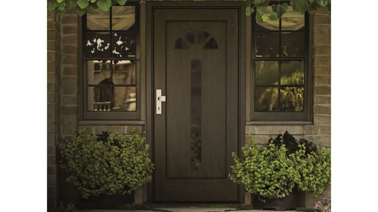 Elegancka aranżacja drzwi wejściowych z ciemnobrązowymi drzwiami, bocznymi oknami i zielonymi roślinami w donicach.