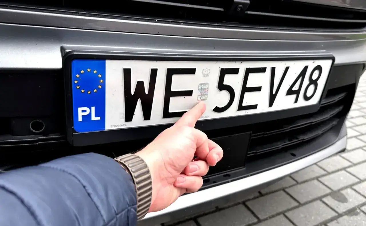 Palec wskazuje hologram na tablicy rejestracyjnej, symbolizujący przyszłe zmiany w opłatach, jak podatek od aut spalinowych.