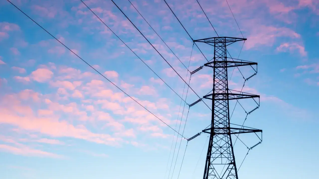 Wieża z przewodami linii energetycznej średniego napięcia na tle r&oacute;żowo-niebieskiego nieba z chmurami.