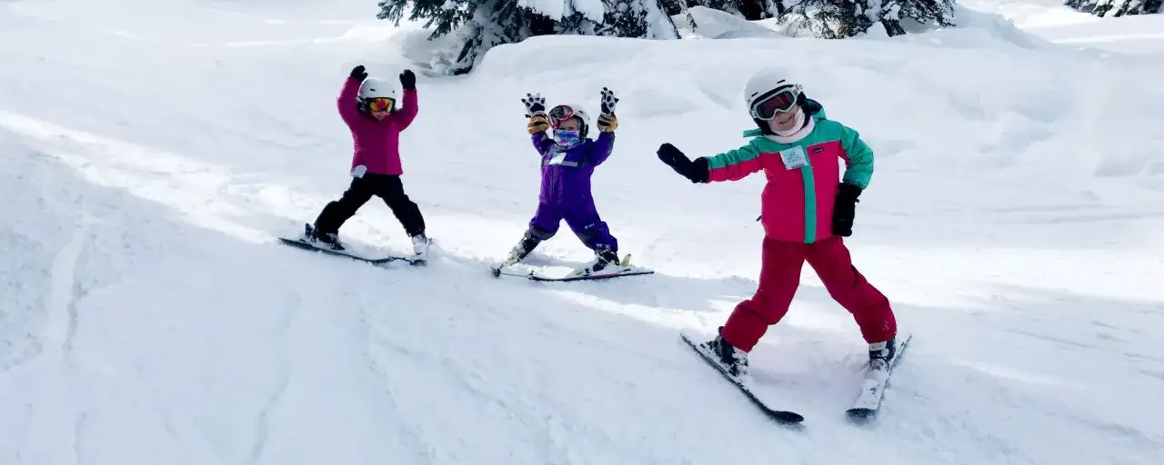 Trzy dzieci na nartach, uczą się jak jeździć na nartach, radośnie machają rękami na stoku.
