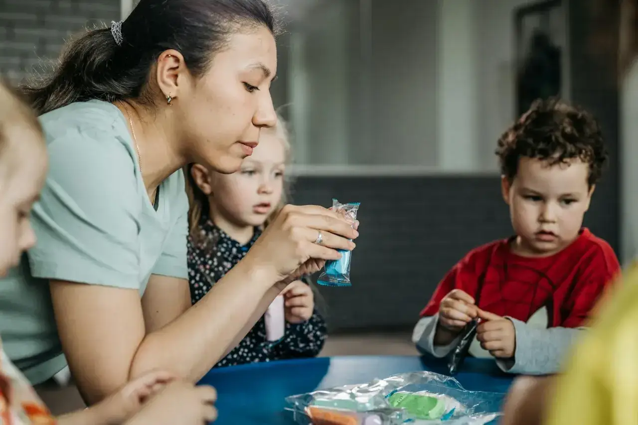 Nauczycielka pomaga dzieciom z lękiem separacyjnym u 5 latka w zajęciach plastycznych. Dzieci skupione na masie plastycznej.