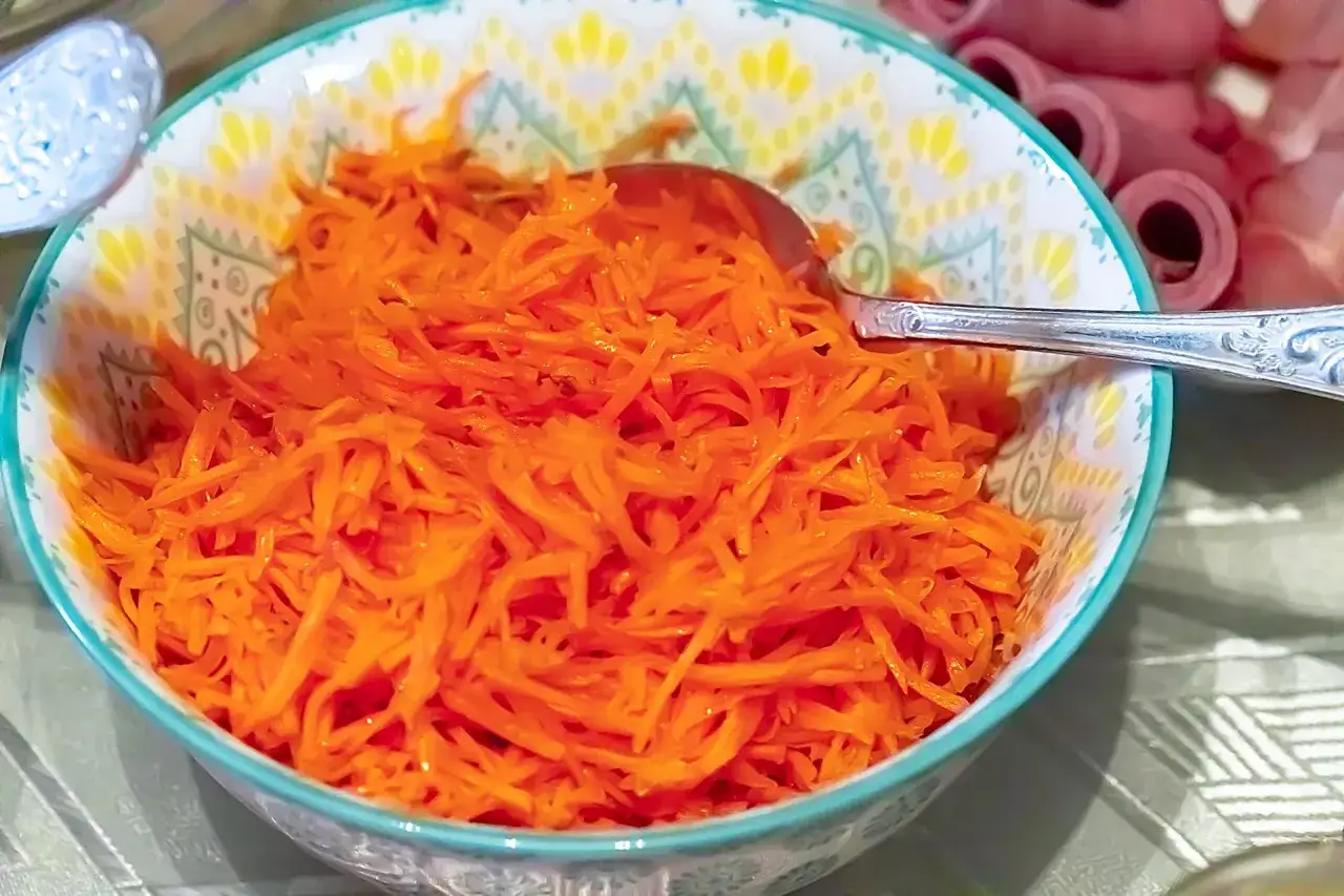 Surówka z marchewki i jabłka w misce, obok rolki wędliny. Idealna alternatywa dla buraczków zasmażanych.