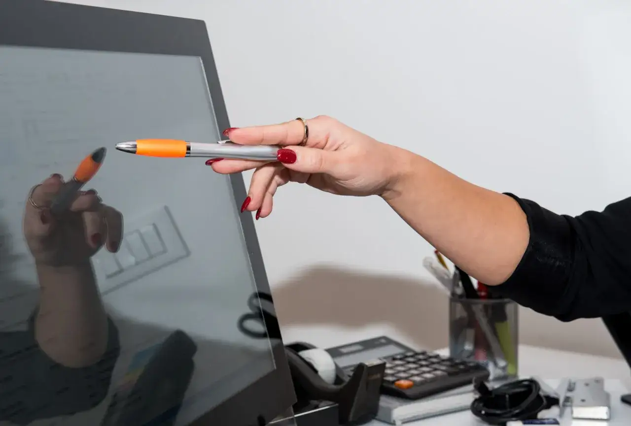 Dłoń z pomarańczowym długopisem wskazuje na ekran, ilustrując, jak będzie wyglądało nauczanie hybrydowe.