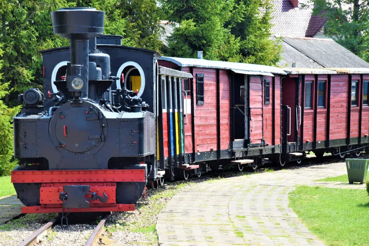 Czarna lokomotywa i czerwone wagony stoją na torach. Ten zabytkowy szlak kolejki wąskotorowej zaprasza do podróży w przeszłość.