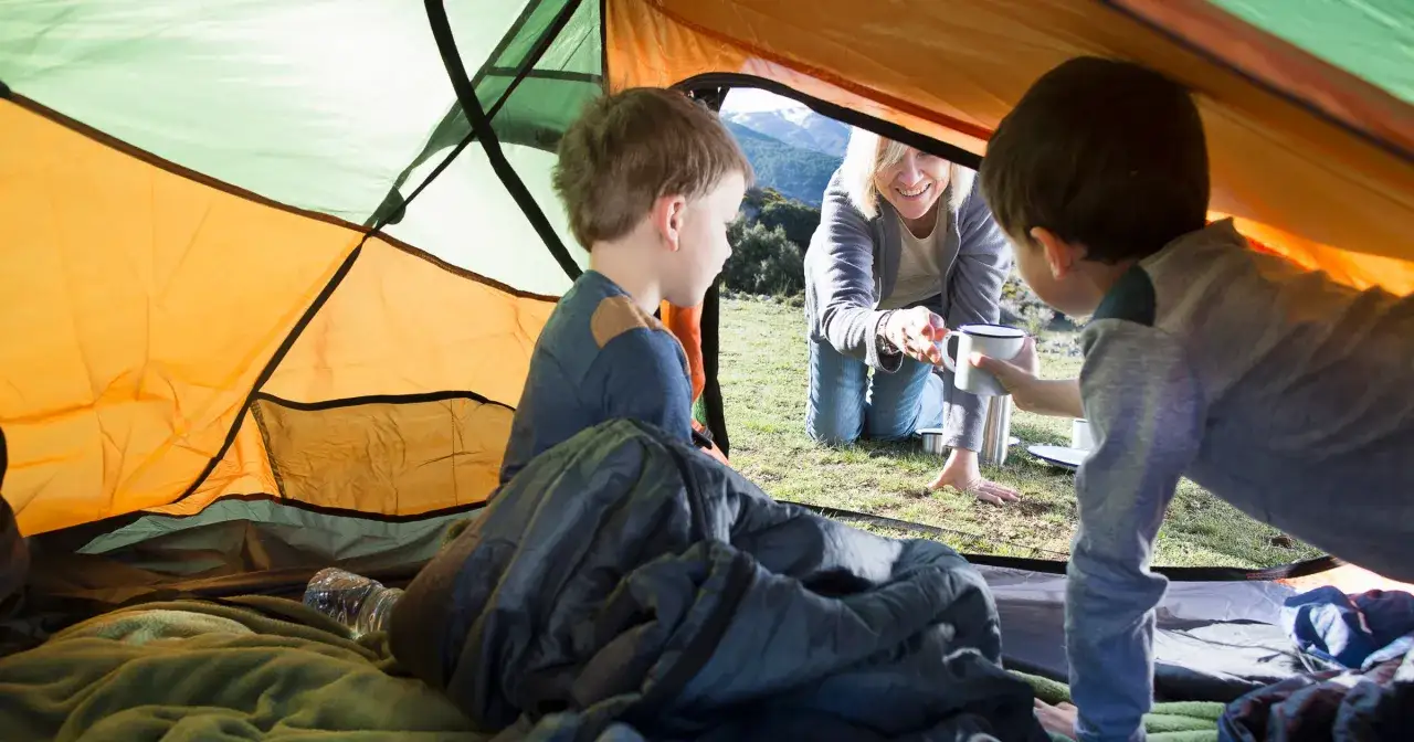 Wesoła rodzina w namiocie, przygotowująca się do przygody. Pomyśl, co zabrać pod namiot z dziećmi, by było równie miło!