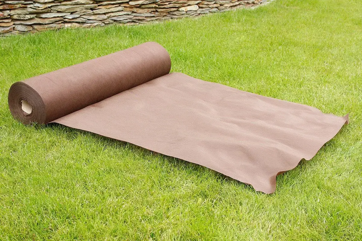 Brązowa agrowł&oacute;knina na chwasty rozwinięta na trawniku. Idealna do ogrodu, by zapobiec niechcianym roślinom.