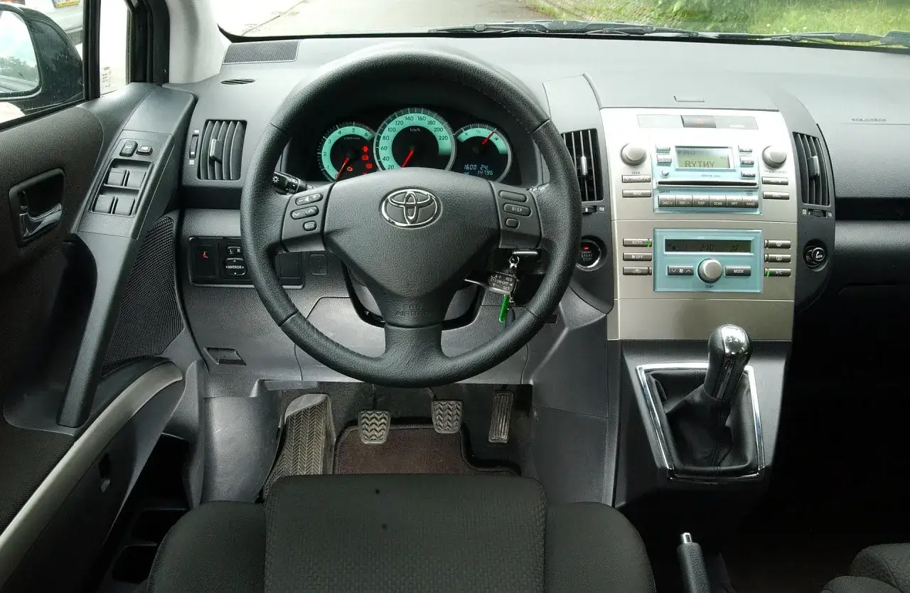 Wnętrze Toyoty Verso: kierownica, deska rozdzielcza z radiem i panelem klimatyzacji, dźwignia zmiany biegów.