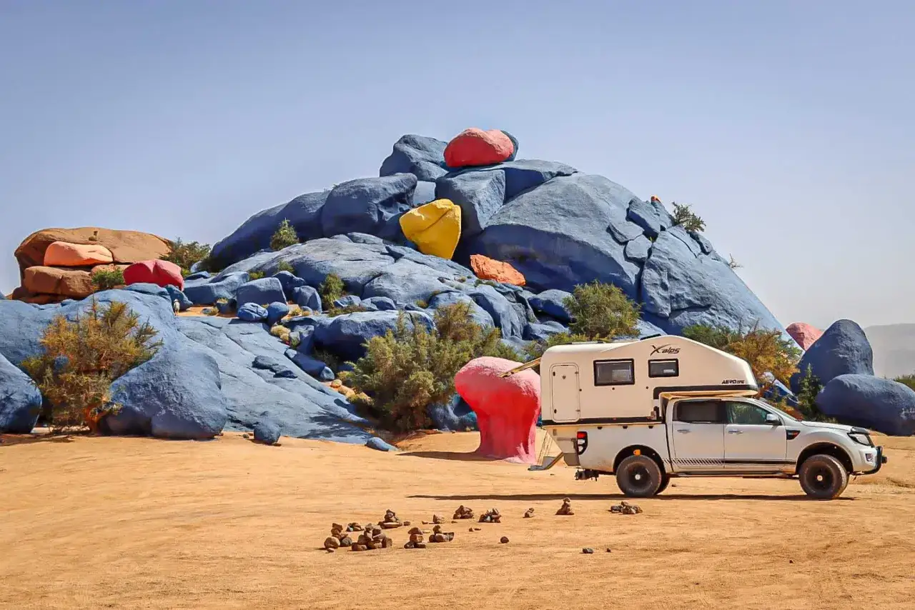 Biały van camper zaparkowany na pustyni obok kolorowych skał.