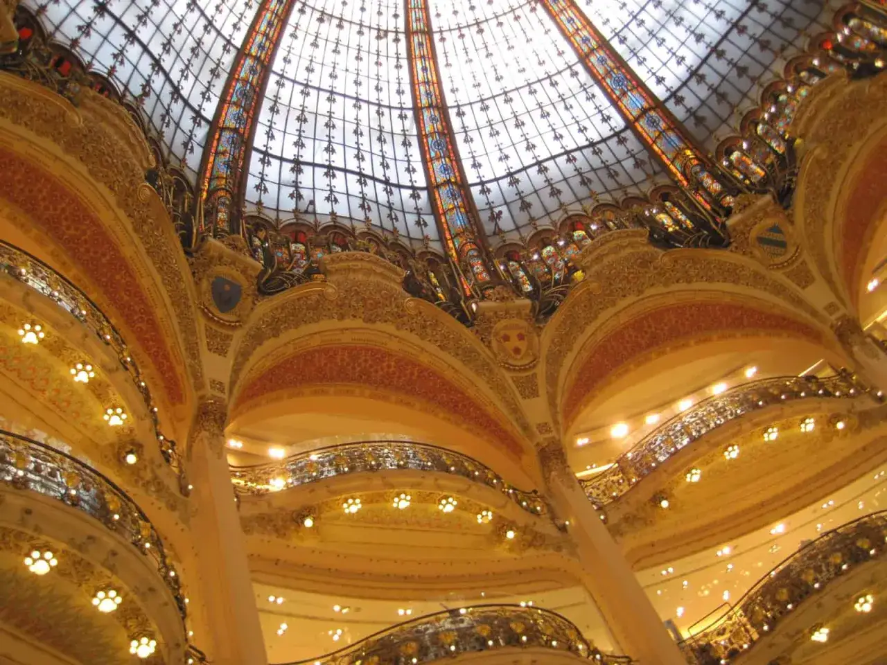 Wnętrze Galerii Lafayette w 9. dzielnicy Paryża. Wspaniała, witrażowa kopuła i złote zdobienia tworzą magiczną atmosferę.
