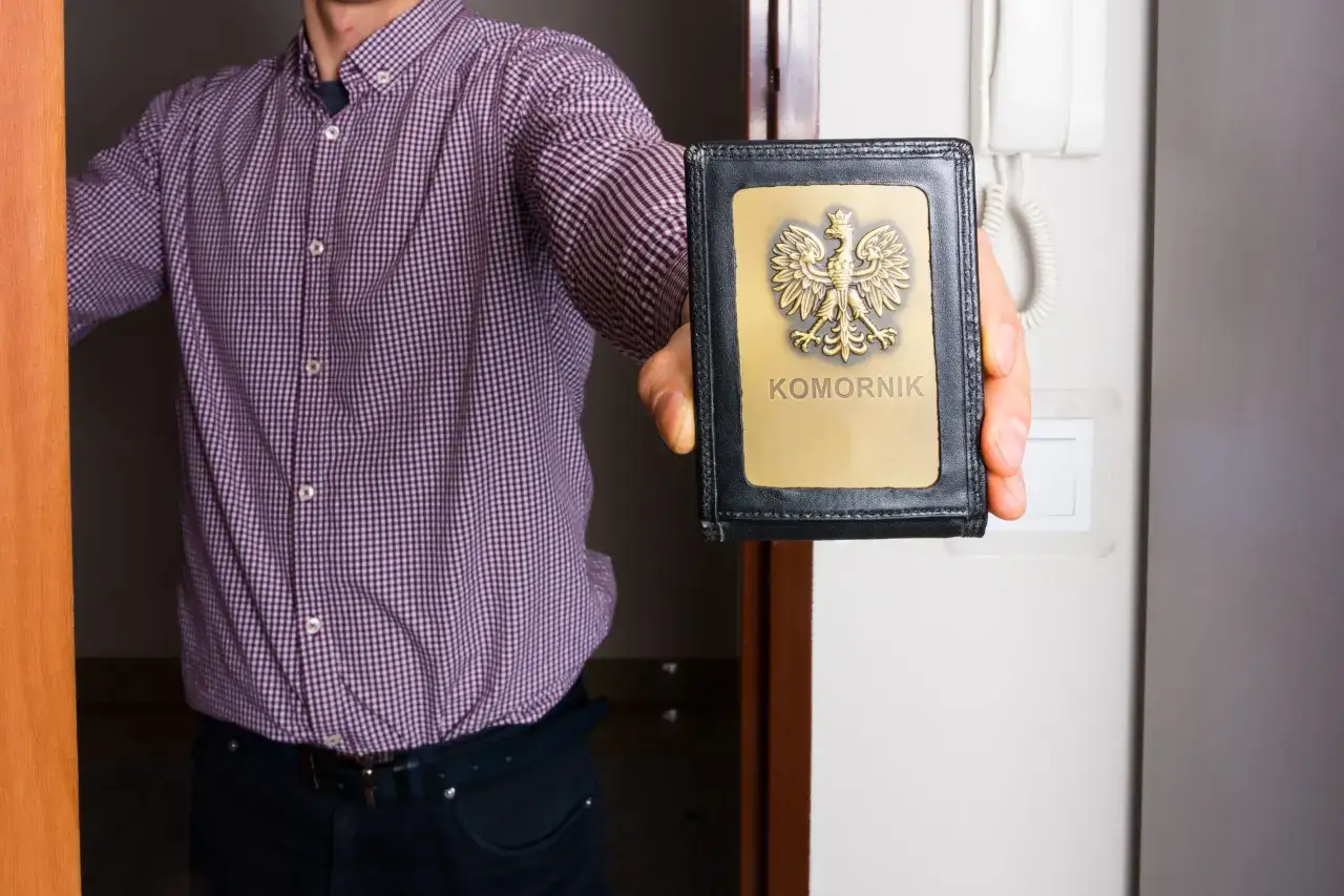 Mężczyzna w kratę pokazuje legitymację, gdy komornik przychodzi do domu.