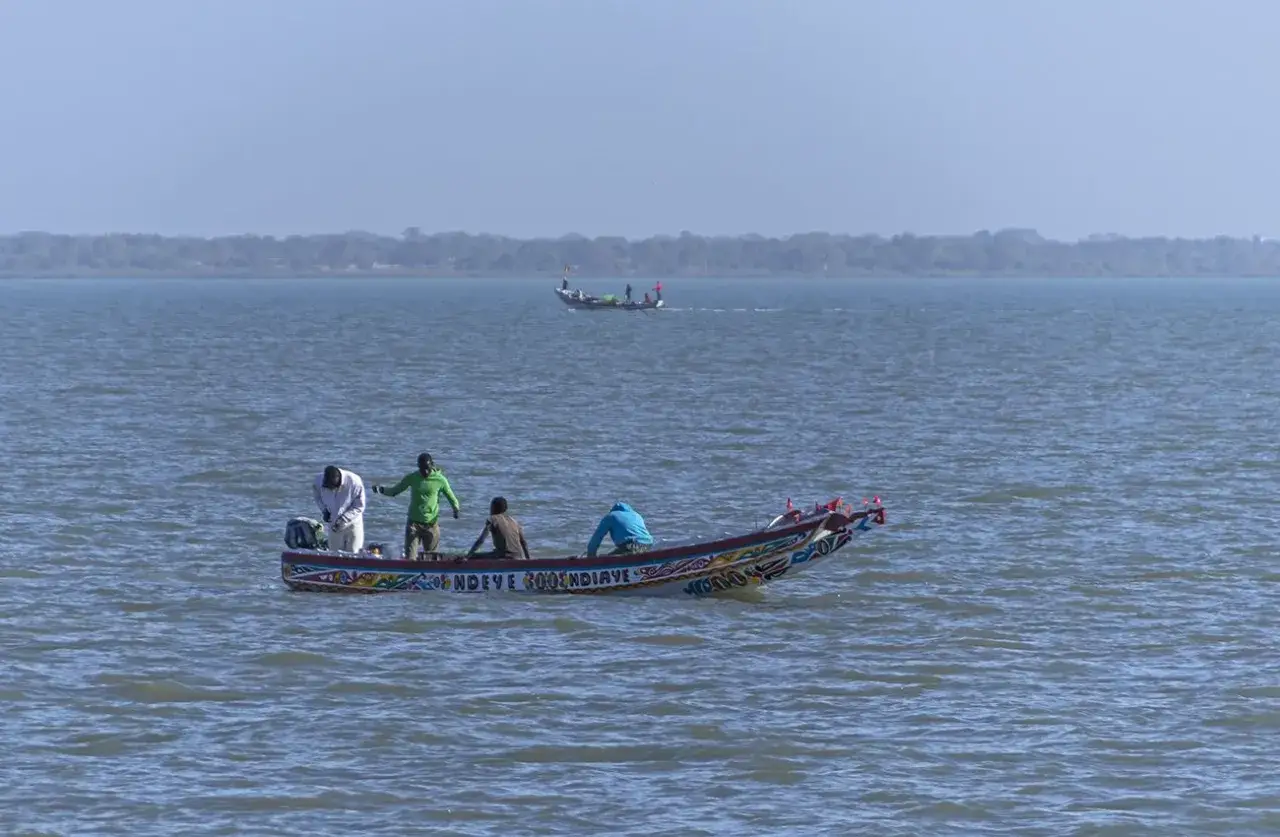 Łódź rybacka z kolorowymi zdobieniami płynie po rzece Gambia. Na pokładzie widać kilku mężczyzn.