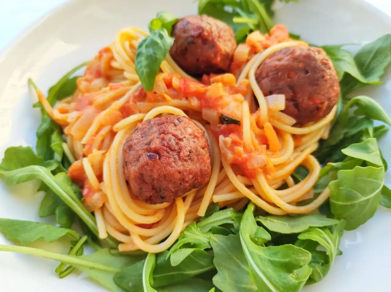 Pyszne spaghetti z pulpetami w sosie pomidorowym, udekorowane świeżą rukolą i listkami bazylii.