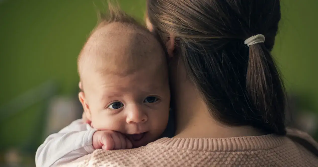 Maluch wtulony w ramię mamy, z zaciekawieniem spogląda na świat. Czyżby to pierwsze objawy ząbkowania tr&oacute;jki?